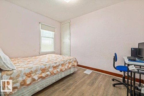 Bedroom featuring wood-finish flooring, a window with roller shade, and a built-in closet with a paneled door - 10939 96 Street, Edmonton, AB - Indoor Photo Showing Bedroom