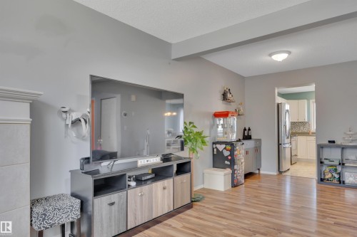 Spacious living area featuring light gray walls, wood-finish flooring, and a fireplace with a white mantel - 102 4415 South Park Drive, Leduc, AB - Indoor