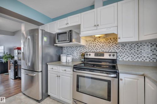 Kitchen featuring stainless steel appliances, white cabinetry, light-toned countertops, and a patterned tile backsplash - 102 4415 South Park Drive, Leduc, AB - Indoor Photo Showing Kitchen