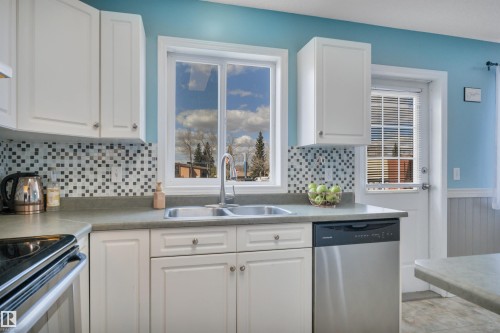 Kitchen featuring white cabinetry, a dual-basin stainless steel sink with a gooseneck faucet, a mosaic tile backsplash, a stainless steel dishwasher, and a window above the sink - 102 4415 South Park Drive, Leduc, AB - Indoor Photo Showing Kitchen With Double Sink