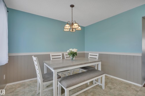 Dining area featuring wainscoting with decorative trim, a textured ceiling, and a traditional chandelier - 102 4415 South Park Drive, Leduc, AB - Indoor Photo Showing Dining Room