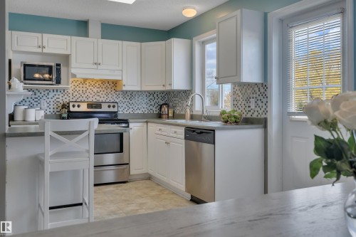 Kitchen featuring white cabinetry, mosaic tile backsplash, stainless steel appliances, and solid surface countertops - 102 4415 South Park Drive, Leduc, AB - Indoor Photo Showing Kitchen
