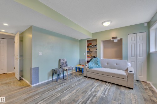Spacious room featuring wood-finish flooring, light green walls, a built-in shelving unit, and bifold closet doors - 102 4415 South Park Drive, Leduc, AB - Indoor Photo Showing Bedroom