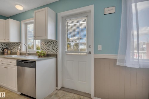 Kitchen featuring white cabinetry, a stainless steel dishwasher, a mosaic tile backsplash, and a double-basin sink with a gooseneck faucet - 102 4415 South Park Drive, Leduc, AB - Indoor Photo Showing Kitchen