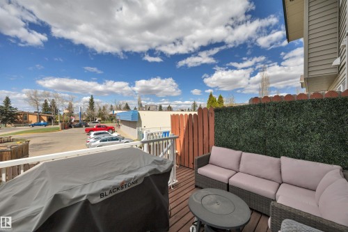 Wood-finish deck with white railing, featuring a faux-hedge privacy screen, and a red-stained wood fence - 102 4415 South Park Drive, Leduc, AB - Outdoor With Deck Patio Veranda