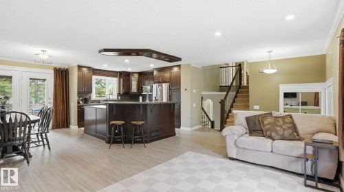 Open-concept living space with light-toned wood-finish flooring, dark wood cabinetry, and stainless steel appliances - 27 Addison Crescent, St. Albert, AB - Indoor