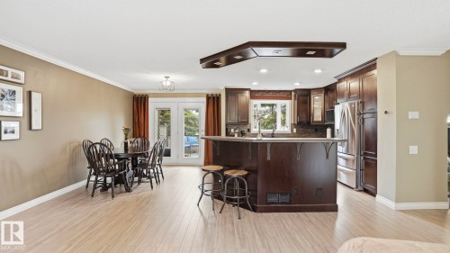 Open-concept living space featuring wood-finish flooring, a kitchen island with seating, dark wood cabinetry, and stainless steel appliances - 27 Addison Crescent, St. Albert, AB - Indoor