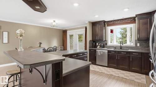Kitchen featuring dark wood cabinetry, a large kitchen island with seating, stainless steel appliances, a bay window, and light wood-finish flooring - 27 Addison Crescent, St. Albert, AB - Indoor Photo Showing Kitchen