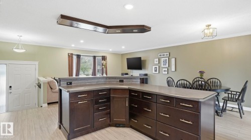 Spacious open-concept interior featuring a large kitchen island with dark cabinetry and light countertops, wood-finish flooring, and recessed ceiling lighting - 27 Addison Crescent, St. Albert, AB - Indoor
