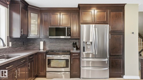 Kitchen featuring dark wood cabinetry, stainless steel appliances, a tile backsplash, and light-toned countertops - 27 Addison Crescent, St. Albert, AB - Indoor Photo Showing Kitchen With Upgraded Kitchen