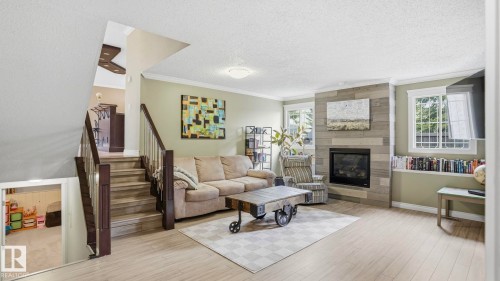 Living area featuring wood-finish flooring, a stone-accented fireplace, and built-in shelving - 27 Addison Crescent, St. Albert, AB - Indoor Photo Showing Living Room With Fireplace
