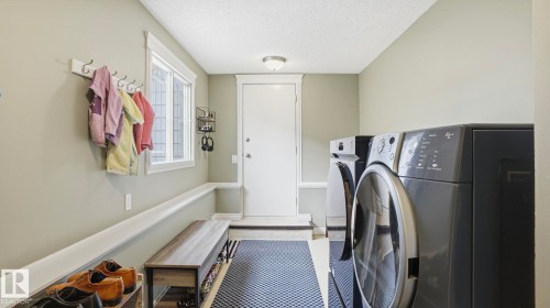 Functional utility room featuring a front-loading washer and dryer, window, wall-mounted coat rack, and a built-in bench - 27 Addison Crescent, St. Albert, AB - Indoor Photo Showing Laundry Room