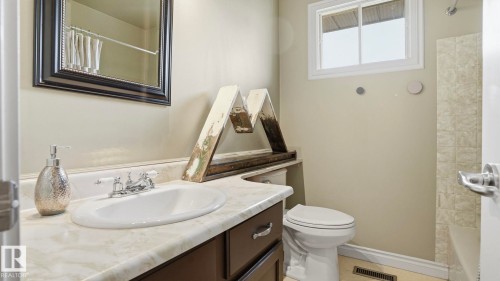 Bathroom featuring a white oval undermount sink, a chrome two-handle faucet, a vanity with a light-colored countertop, and a built-in toilet - 27 Addison Crescent, St. Albert, AB - Indoor Photo Showing Bathroom