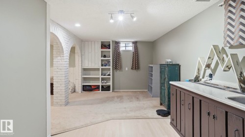 Spacious lower level featuring light-toned walls, built-in shelving, carpeted and wood-finish flooring, and a wet bar with dark cabinetry - 27 Addison Crescent, St. Albert, AB - Indoor