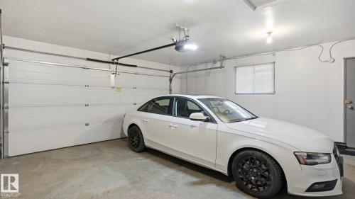Attached garage featuring a white overhead door, concrete flooring, overhead lighting, and a side window - 27 Addison Crescent, St. Albert, AB - Indoor Photo Showing Garage