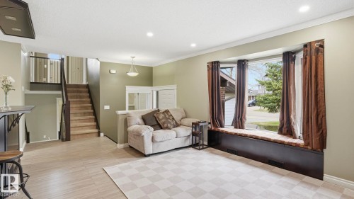 Spacious living area featuring a large bay window with a built-in window seat, recessed lighting, wood-finish flooring, and a carpeted staircase with dark wood railings - 27 Addison Crescent, St. Albert, AB - Indoor