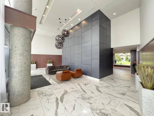 Lobby area featuring large format marble-look tile flooring, a dark accent wall with panel detailing, and contemporary spherical chandeliers - 710 2504 109 Street Nw, Edmonton, AB 