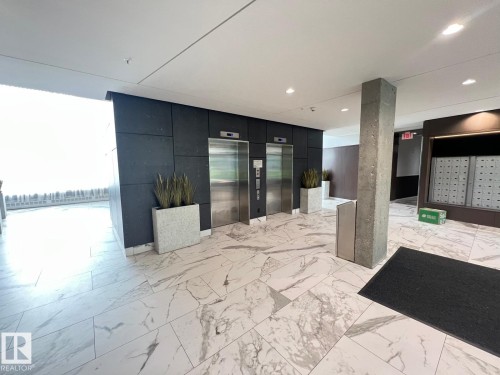Lobby area featuring two stainless steel elevators, white marble-look flooring, dark wall paneling, and a mailroom with individual mailboxes - 710 2504 109 Street Nw, Edmonton, AB 