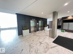 Lobby area featuring two stainless steel elevators, white marble-look flooring, dark wall paneling, and a mailroom with individual mailboxes - 
