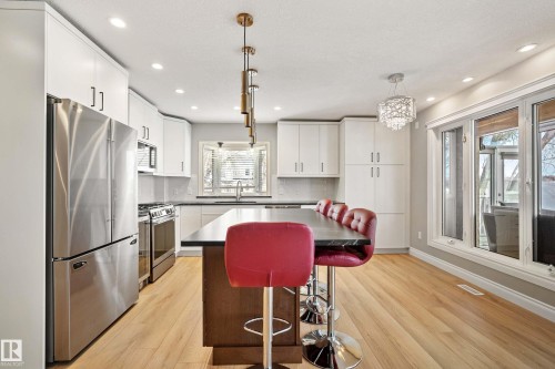 Contemporary kitchen featuring wood-finish flooring, white cabinetry, dark countertops, a stainless steel refrigerator, and a kitchen island with seating - 104 Bayview Drive, Rural Parkland County, AB - Indoor Photo Showing Kitchen With Upgraded Kitchen
