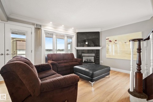 Living area featuring light wood-finish flooring, a corner fireplace with a dark stone surround and white mantel, and crown molding - 104 Bayview Drive, Rural Parkland County, AB - Indoor Photo Showing Living Room With Fireplace