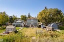 Waterfront property featuring two structures, established landscaping, a ground-level patio, an upper-level deck with glass railings, and a detached storage shed - 104 Bayview Drive, Rural Parkland County, AB  - Outdoor With Deck Patio Veranda 