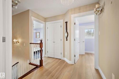 Upper landing featuring wood-finish flooring, white spindle railing with dark wood banister, and an ornate crystal chandelier - 104 Bayview Drive, Rural Parkland County, AB - Indoor Photo Showing Other Room
