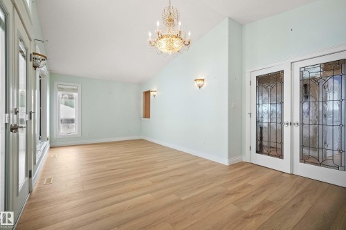 Spacious room featuring wood-finish flooring, a vaulted ceiling with a prominent chandelier, and multiple French doors - 104 Bayview Drive, Rural Parkland County, AB - Indoor Photo Showing Other Room