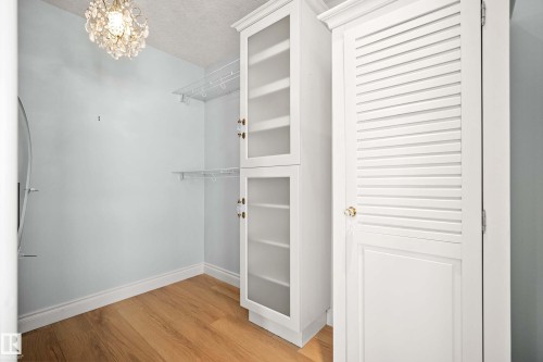 Custom closet system featuring white cabinetry with frosted glass doors, a louvered door cabinet, wire shelving, and wood-finish flooring - 104 Bayview Drive, Rural Parkland County, AB - Indoor Photo Showing Other Room