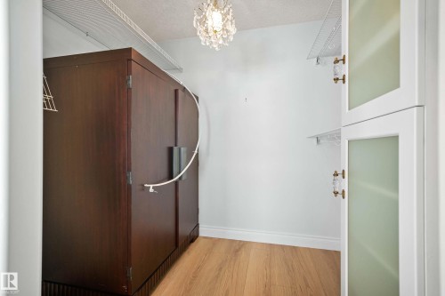Custom closet featuring a large dark wood-finish armoire, wood-finish flooring, white wire shelving, and a decorative chandelier - 104 Bayview Drive, Rural Parkland County, AB - Indoor Photo Showing Other Room