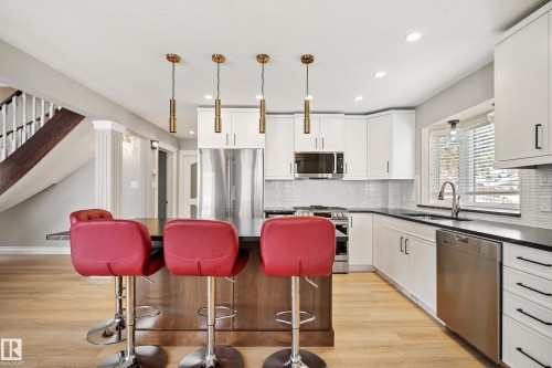 Kitchen featuring a central island with counter seating, stainless steel appliances, white cabinetry, dark countertops, and light wood-finish flooring - 104 Bayview Drive, Rural Parkland County, AB - Indoor Photo Showing Kitchen With Upgraded Kitchen