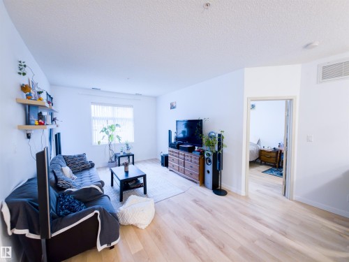 Spacious living area featuring light wood-finish flooring, white walls, and a large window with horizontal blinds - 135 7825 71 Street, Edmonton, AB - Indoor Photo Showing Living Room