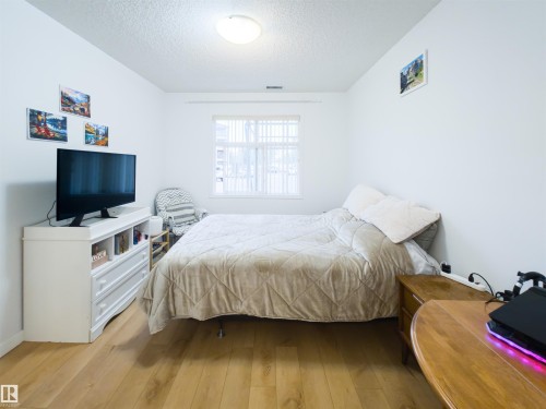 Bright interior room featuring wood-finish flooring, a contemporary window with blinds, a white ceiling light fixture, and white painted walls - 135 7825 71 Street, Edmonton, AB - Indoor Photo Showing Bedroom