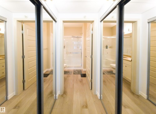 Hallway featuring light wood-finish flooring, two sets of mirrored sliding closet doors, and multiple entryways - 135 7825 71 Street, Edmonton, AB - Indoor Photo Showing Other Room