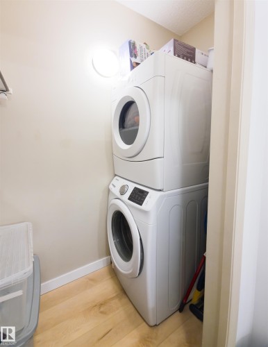 Dedicated laundry area featuring light wood-finish flooring and a stacked washer and dryer unit - 135 7825 71 Street, Edmonton, AB - Indoor Photo Showing Laundry Room