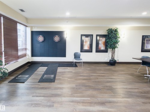 Party room featuring two dartboards on a dark accent wall, wood-finish flooring, recessed lighting, and large windows with horizontal blinds - 135 7825 71 Street, Edmonton, AB - Indoor Photo Showing Other Room