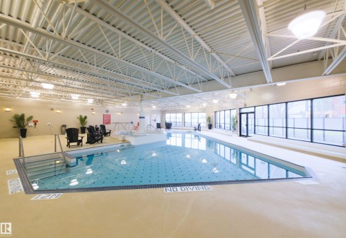 Indoor swimming pool featuring a spa, multiple entry points, and expansive window walls - 135 7825 71 Street, Edmonton, AB - Indoor Photo Showing Other Room With In Ground Pool