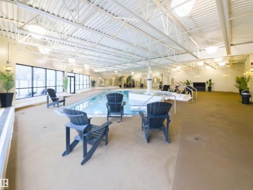 Indoor pool facility featuring a large rectangular pool, wide concrete decking, and expansive windows - 135 7825 71 Street, Edmonton, AB - Indoor Photo Showing Other Room With In Ground Pool