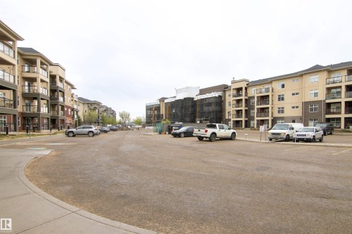 Property exterior featuring multi-story buildings with balconies, light-colored facades, dark trim, and a paved parking area - 135 7825 71 Street, Edmonton, AB - Outdoor With Facade