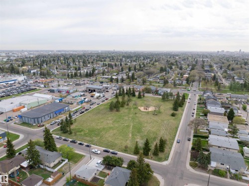 Aerial perspective showcasing the surrounding neighborhood, featuring residential homes, commercial buildings, and a central green space with scattered trees - 135 7825 71 Street, Edmonton, AB - Outdoor With View