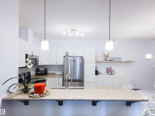Kitchen featuring white cabinetry, stainless steel appliances, a double basin sink, and a speckled countertop - 135 7825 71 Street, Edmonton, AB - Indoor Photo Showing Kitchen With Upgraded Kitchen