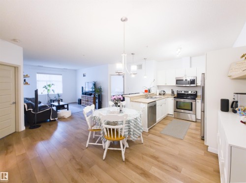 Open-concept living space featuring wood-finish flooring, a kitchen with stainless steel appliances, white cabinetry, and light-toned countertops - 135 7825 71 Street, Edmonton, AB - Indoor