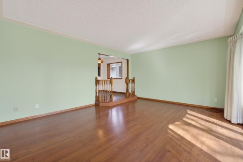 Spacious room featuring wood-finish flooring, light green walls with white trim, and a window with vertical blinds - 12016 51 Street, Edmonton, AB - Indoor Photo Showing Other Room