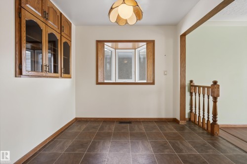 Recessed wooden cabinetry with glass inserts, a bay window with natural wood trim, and a decorative ceiling light fixture - 12016 51 Street, Edmonton, AB - Indoor Photo Showing Other Room