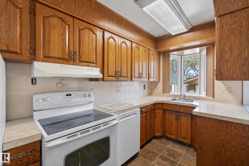 Kitchen featuring abundant wood-finish cabinetry, a white electric range, and a bay window above the sink - 12016 51 Street, Edmonton, AB - Indoor Photo Showing Kitchen