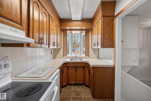 Galley kitchen featuring wood-finish cabinetry, a bay window, and a tiled backsplash - 12016 51 Street, Edmonton, AB - Indoor