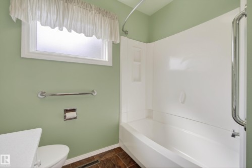 Bathroom featuring a white tub-shower combination with integrated shelving, a white toilet, and wood-finish flooring - 12016 51 Street, Edmonton, AB - Indoor Photo Showing Bathroom