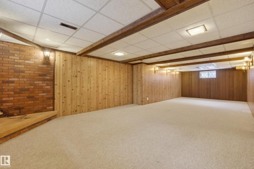 Spacious finished basement featuring a brick accent wall, wood paneling, exposed wood beams, and recessed lighting - 12016 51 Street, Edmonton, AB - Indoor Photo Showing Basement