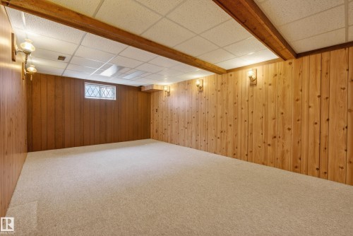 Spacious room featuring light wood paneling, exposed wood beams, and neutral carpeting - 12016 51 Street, Edmonton, AB - Indoor