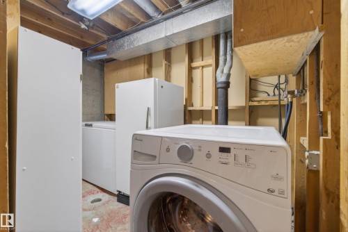 Dedicated utility space featuring a front-load washing machine, exposed wooden joists, and visible ductwork - 12016 51 Street, Edmonton, AB - Indoor Photo Showing Laundry Room